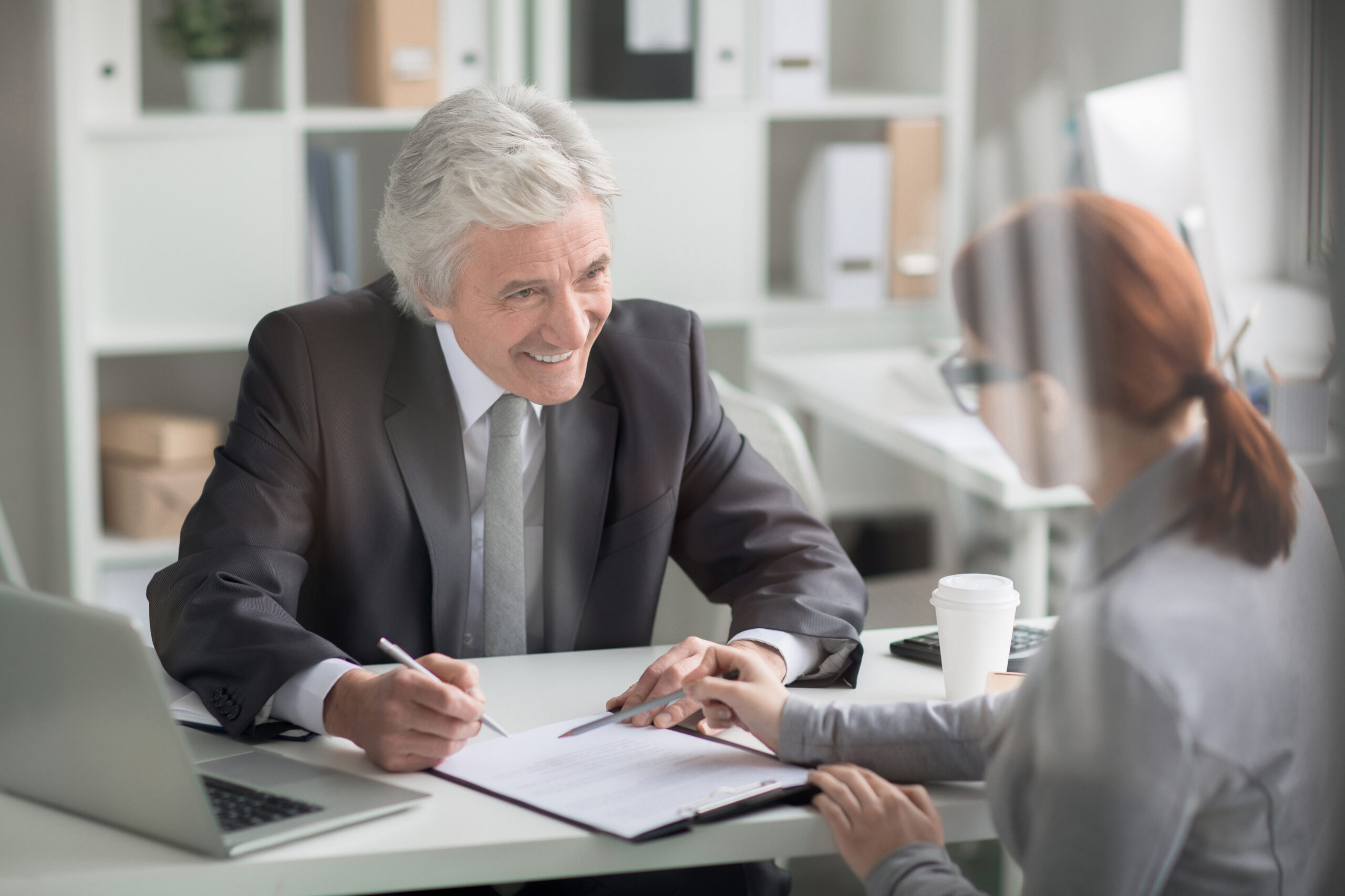 Mature boss looking at young manager with smile while listening to her explanations of report details