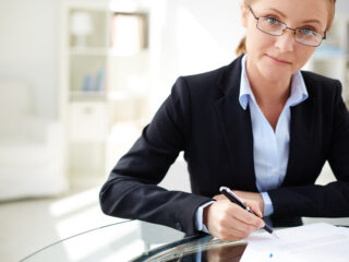Young businesswoman signing contract and looking at camera in office