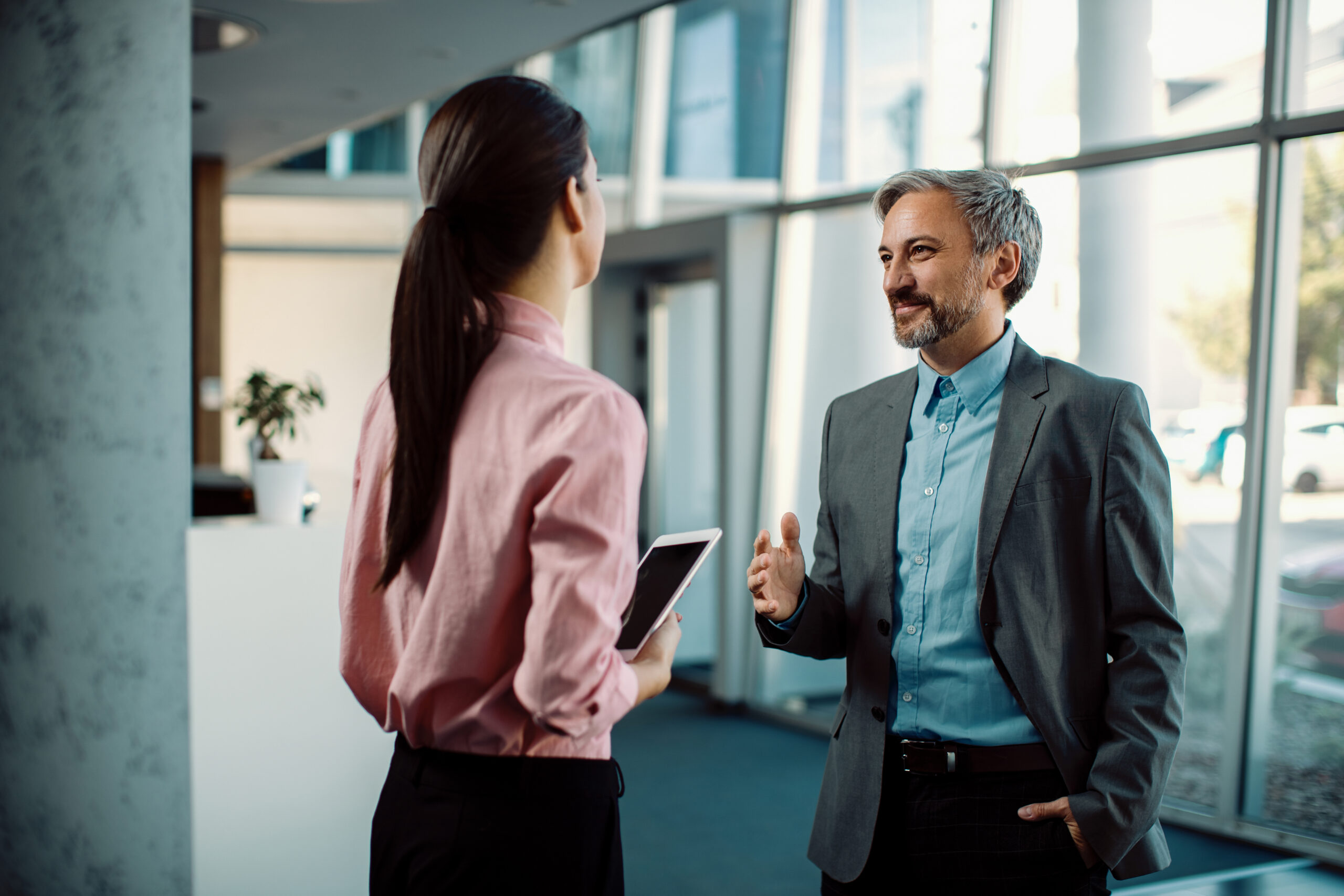 Happy businessman talking to his female colleague in a hallway. Happy mid adult entrepreneur and his female coworker communicating while standing in a lobby.